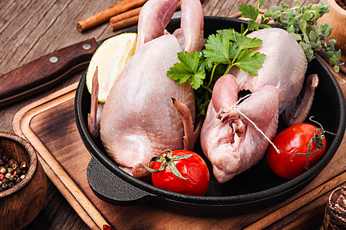 Fresh raw quail on kitchen board in iron cast pan.Quail meat