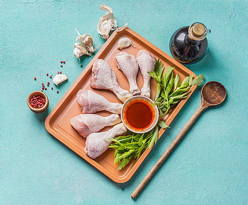 Cooking preparation of raw chicken drumsticks. Raw Chicken legs on plate with herbs, spices , sauce and cooking spoon on light blue background, top view