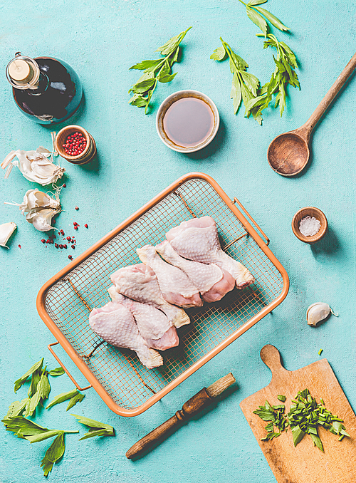 Cooking preparation of raw chicken drumsticks. Raw Chicken legs on grill steel grid with ingredients,  herbs, spices , sauce and cooking spoon on light blue kitchen table background, top view