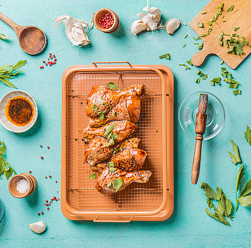 Cooking preparation of raw chicken drumsticks. Raw marinated Chicken legs on grill grid with ingredients,  herbs, spices , sauce and cooking spoon on light blue kitchen table background, top view