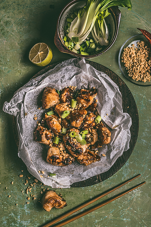 Close up of fried teriyaki chicken pieces with peanut and spring onions on table background with chopsticks and ingredients. Asian food concept