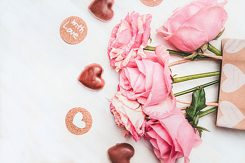 Loving greeting card with pink roses, chocolate with heart symbol  and text with love on white wooden background, top view