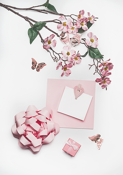 Lovely pastel pink greeting card mock up with blossom decoration, hearts, little gift box and bow on white desk background, top view, flat lay. Wedding invitation  layout or Mother Day  concept