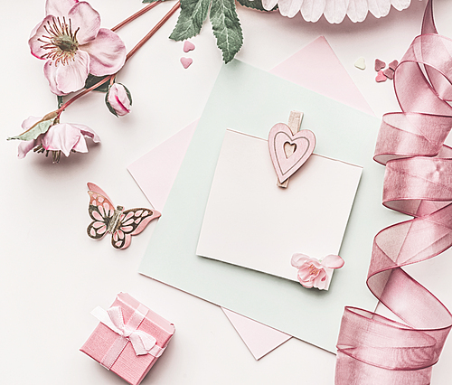 Beautiful pastel pink layout with flowers decoration,ribbon, hearts and card mock up on white desk background, top view, flat lay. Wedding invitation, girls birthday or Mother Day greeting concept