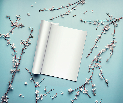 Mock-up of open magazine or catalog on pastel blue desktop with twigs and cherry blossom, top view, flat lay