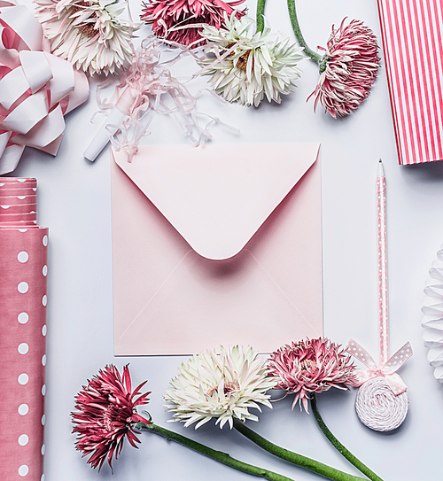Greeting flat lay with pastel pink envelope, pen, flowers, ribbon  and accessories on white desk , top view, flat lay