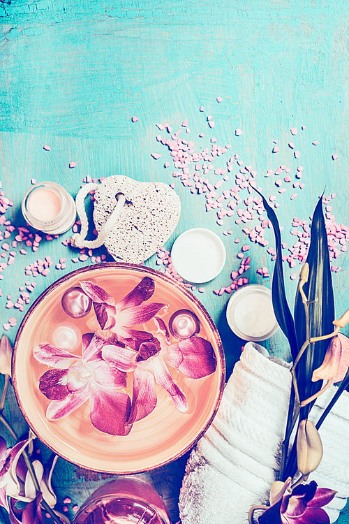 Wellness setting with orchid flowers floating in bowl of water and spa tools on turquoise shabby chic background, top view. Pastel toned