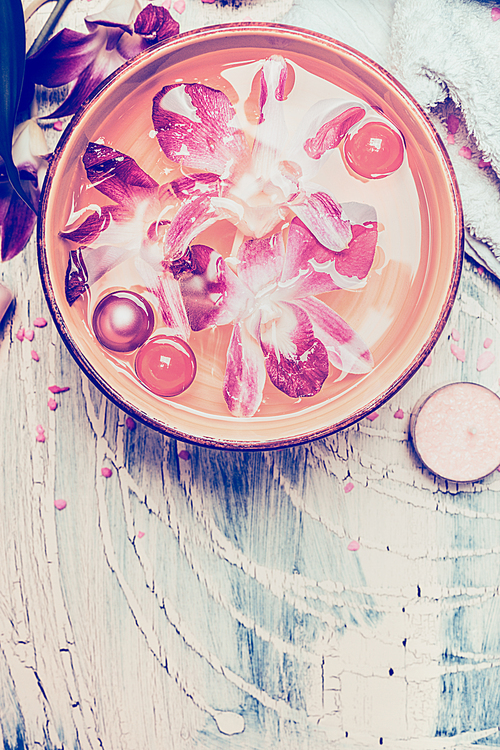 Water bowl with floating orchid flowers and oil balls on light shabby chic wooden background, top view,  pink pastel toned. Spa and Wellness concept