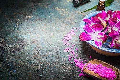 bowl with water and purple orchid flowers on dark background with shovel of 씨솔트. spa, wellness or body care concept.