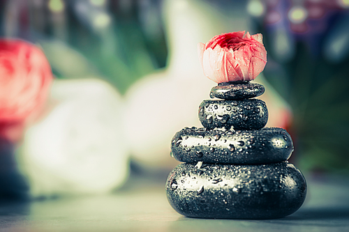 Stack of hot stones with frowers bud at spa wellness background, front view