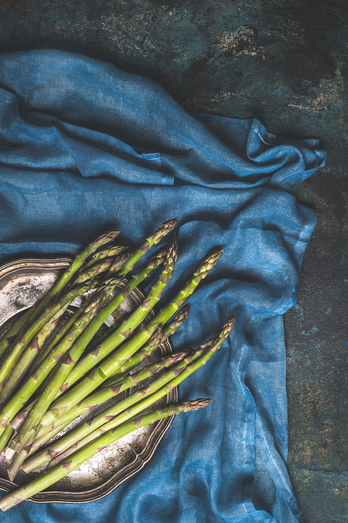 Green asparagus bunch on dark blue rustic background with kitchen towel, top view, place for text.