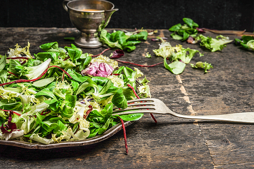 Green leaves mix salad with fork and dressing on rustic kitchen table, close up. Health , detox or diet  food.