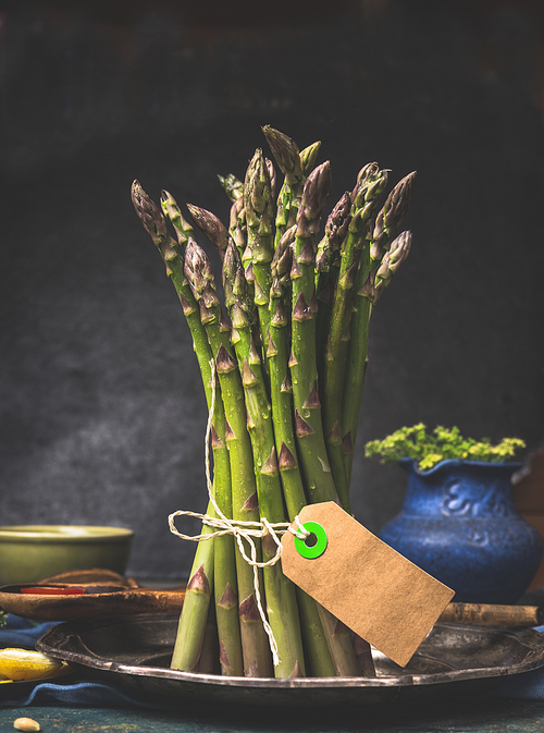 Green asparagus bunch with blank tag standing on dark kitchen table