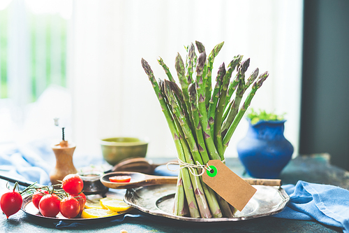 Bunch of green asparagus with cooking vegetables ingredients on kitchen table at window with day light