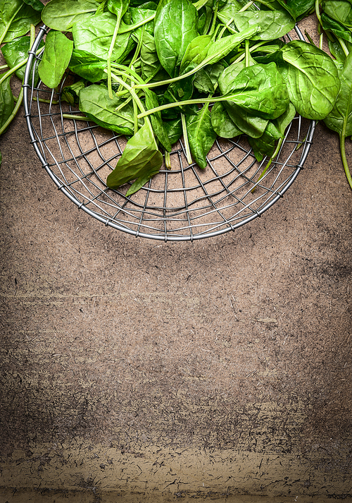Fresh spinach leaves in a metal basket on rustic wooden background, top view