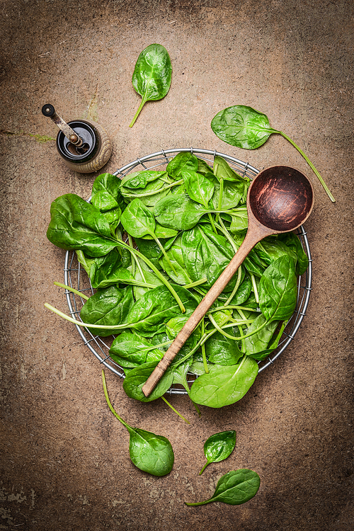 Fresh spinach leaves and wooden spoon on rustic wooden background, top view