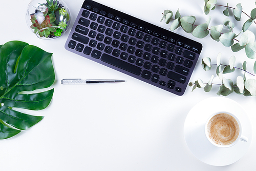 Flat lay home office workspace with black keyboard and green leaves on white background
