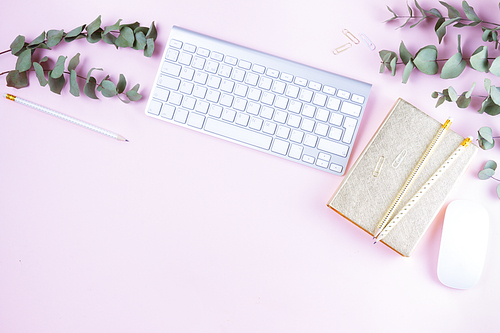 Flat lay home office workspace - white modern keyboard with female accessories and green eucaliptus on pink background