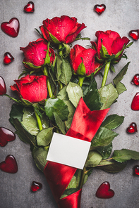 Big flowers bunch with red roses , ribbon ,  blank paper card and hearts on gray background, top view