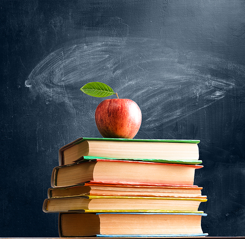 School accessories, books and fresh apple against chalkboard