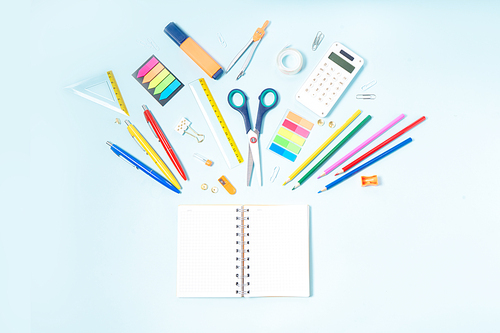 Back to school concept with colorful school supplies on blue background, copy space on ruled paper notebook