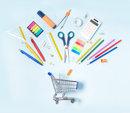 Back to school concept with school supplies falling in cart on blue background with copy space