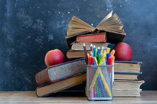 Back to school concept, colorful school supplies with books and red apple on blackboard background with copy space