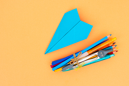 Back to school styled school supplies and blue paper plane on orange background with copy space