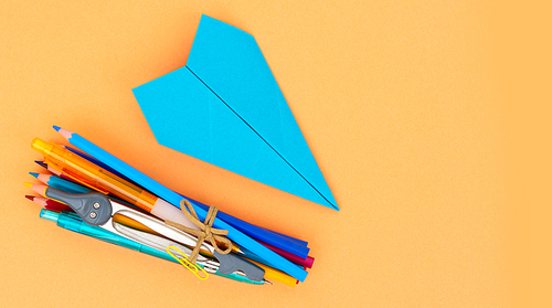 Back to school styled school supplies and blue paper plane on orange background with copy space
