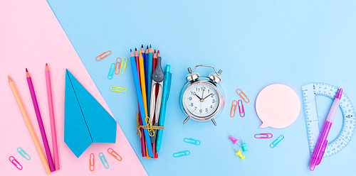 Back to school styled flat lay scene with multicolored school supplies with paper plane on pink and blue background with copy space