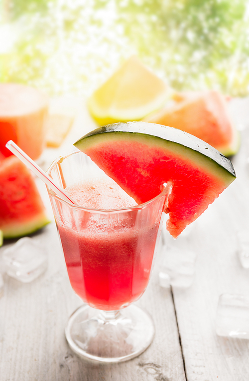 Glass of watermelon juice on rustic wooden table over sunny nature background