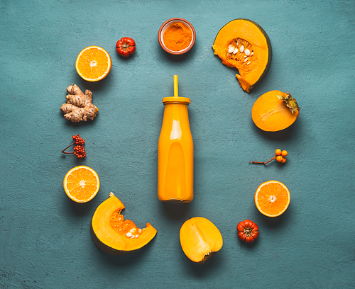 Orange smoothie ingredients : pumpkin, persimmon , orange fruits, ginger and turmeric powder around bottle with healthy energetic smoothie for cold season , top view with copy space for your design