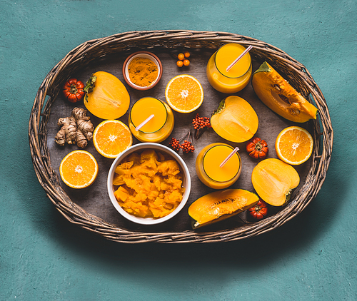 Healthy pumpkin smoothie in glasses with  orange color ingredients : persimmon , orange fruits, ginger and turmeric powder in wooden tray, top view. Immune boosting detox beverage for cold season