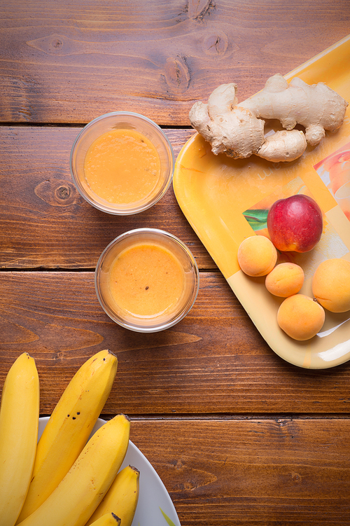 fresh fruit smoothie with banana and apricots at orange  tray  with blender  at wooden table. flat lay