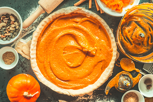 Traditional festive pumpkin pie preparation on rustic kitchen table with cooking tools, top view, retro styled