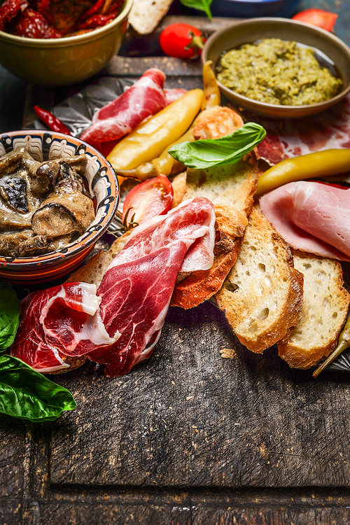 Italian smoked ham Prosciutto with crostini bread and specialties for antipasti on rustic wooden background, close up
