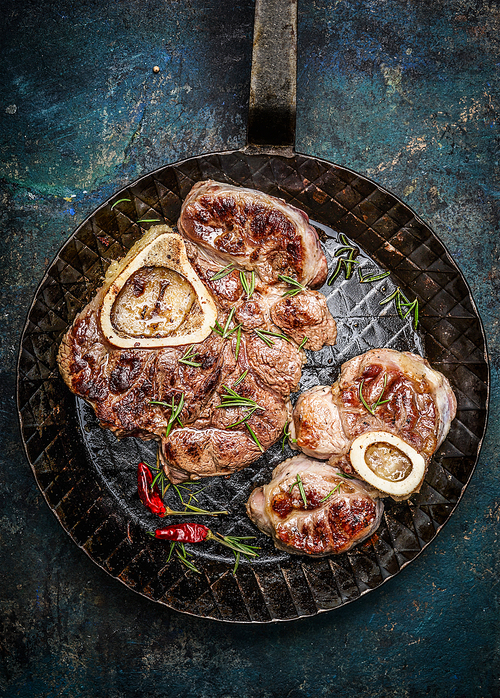 Roasted veal shank slices in frying pan on rustic background, top view, close up