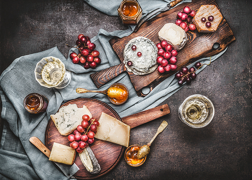 Various cheese served on rustic cutting boards with grape and wine, dark vintage background, top view