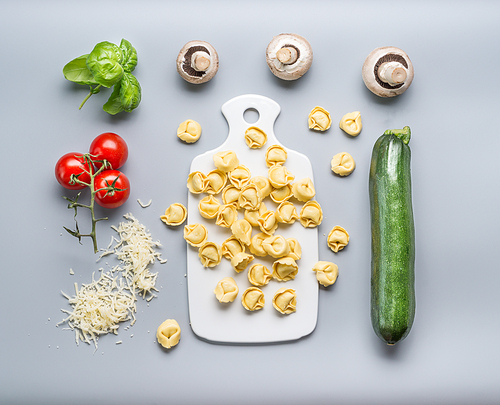 Tortellini with zucchini, mushrooms and vegetarian cooking ingredients on kitchen table background with cutting board , top view, flat lay. Healthy cooking and eating. Italian food concept
