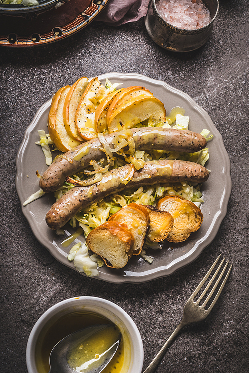 Fried sausages with baked apples, onions and lye bun toast served on rustic table with white coleslaw salad , plates and cutlery  top view, place for text. German food concept