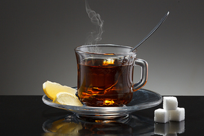 A close up image of a cup of hot tea with a spoon, lemon wedges, and sugar cubes.