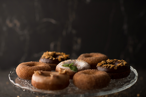 Many different donuts on glass plate on dark stone background
