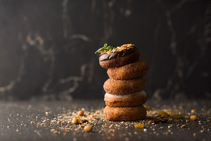 Stack of Donuts with crumbs, nuts and dried fruits on dark stone background