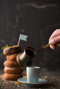 Stack of Donuts with crumbs, nuts and cup of coffee on dark stone background