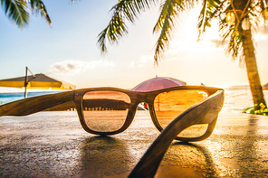 Sunglasses on tropical beach with palms at sunset