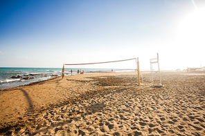 Volleyball net on sunny sandy beach with group of people in the background in summertime