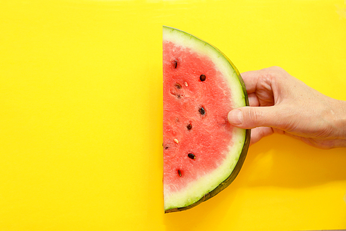 hand holding watermelon slice on yellow background
