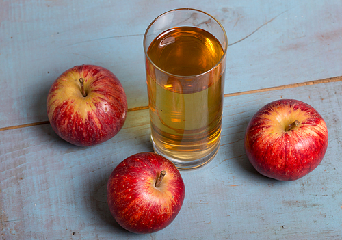 Glass of apple juice and a red apples on a blue old wooden background