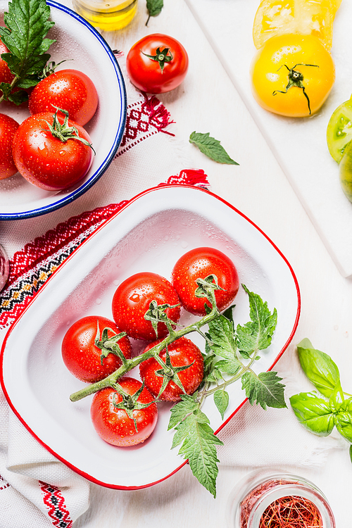 Fresh tasty colorful tomatoes in enamelled bowls on light kitchen table, ready for cooking or salad making, top view.