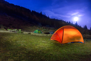 Two Illuminated orange and green camping tents under moon, stars at night